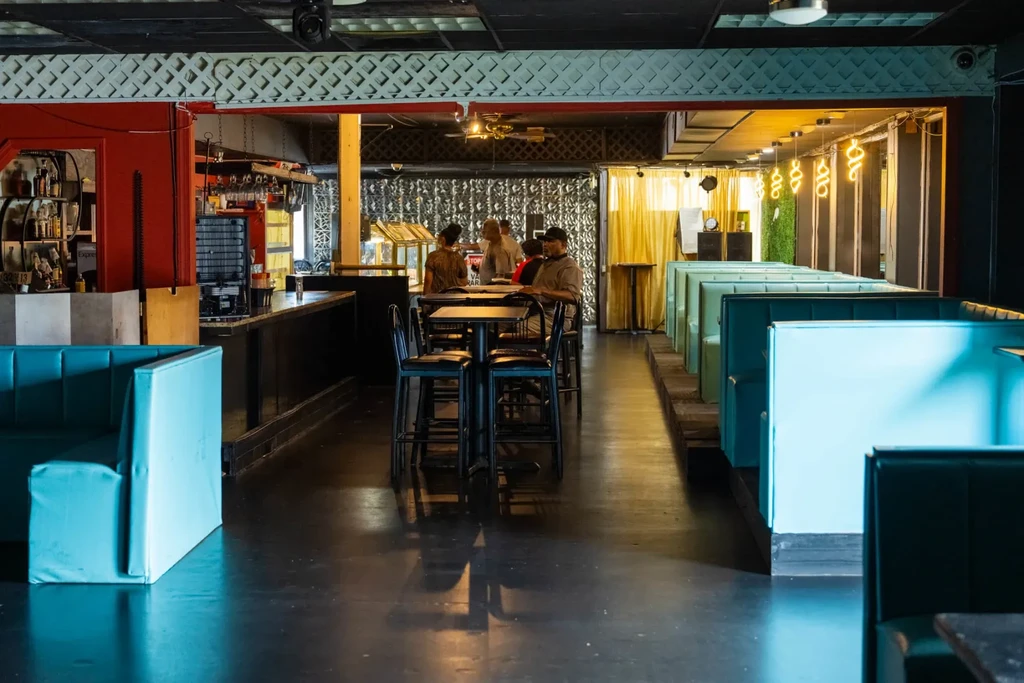 Restaurant interior with teal booths, bar, and occupied high-top tables.
