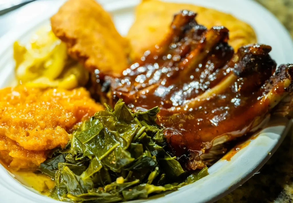 Plate of BBQ ribs, mashed sweet potatoes, and collard greens.
