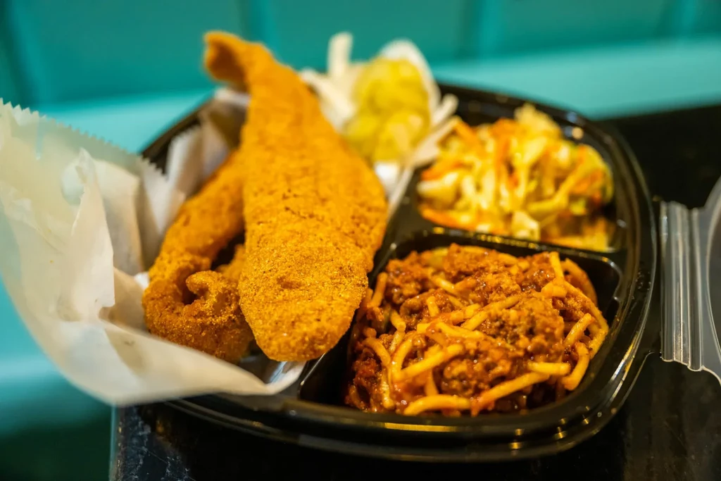 Fried fish, spaghetti, and coleslaw in a take-out container.