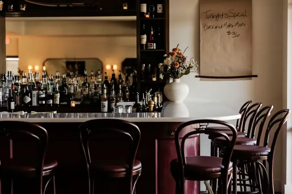 Well-appointed bar with spirits, bar stools, flowers, and a special.