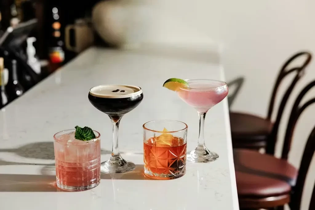 Four distinct cocktails arranged on a light bar counter.
