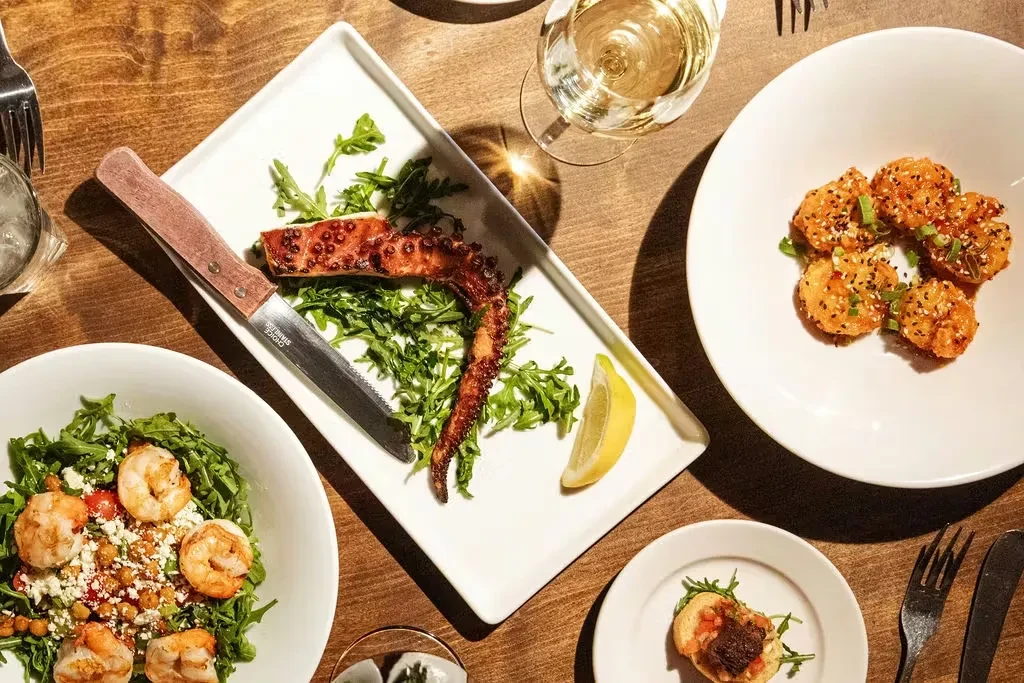 Restaurant table, top-down: grilled octopus, shrimp salad, fried bites, drinks.