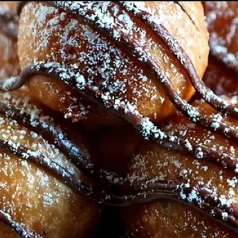 Fried dough pastries with powdered sugar and chocolate sauce.