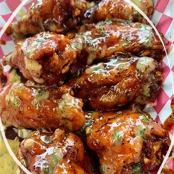 Saucy chicken wings with herbs and white drizzle in a checkered basket.