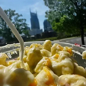 Mac and cheese with sauce pouring, blurred Nashville skyline.