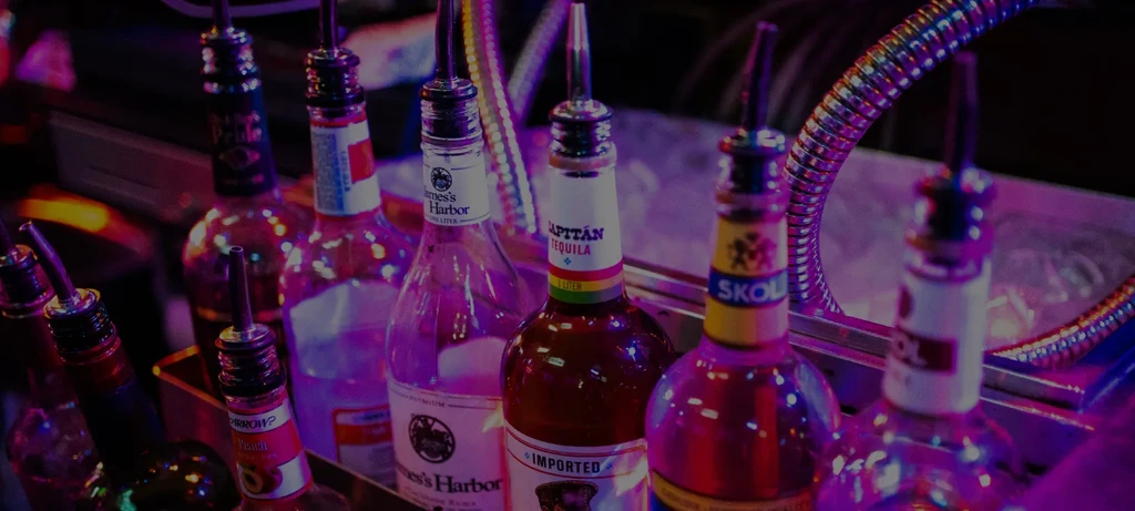Pink and purple neon-lit liquor bottles with pour spouts behind a bar.