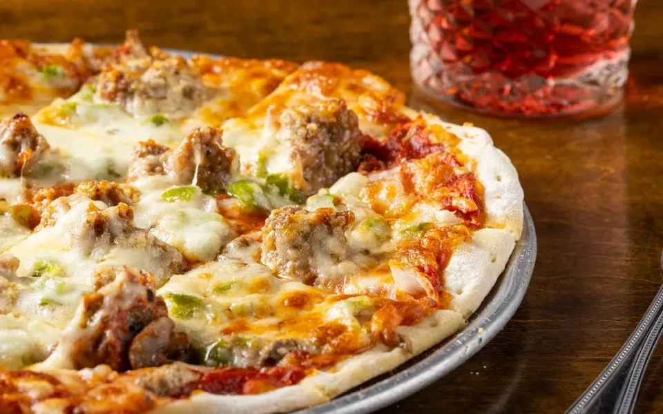 Sausage and green pepper pizza with melted cheese on a metal pan.