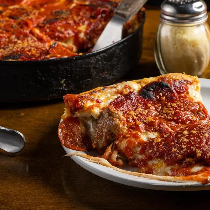 Deep-dish pizza slice with melted cheese, pepperoni, and rich red sauce.