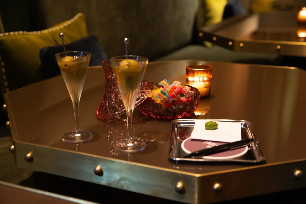 Two martinis, gummies, and a candle on a reflective bar table.