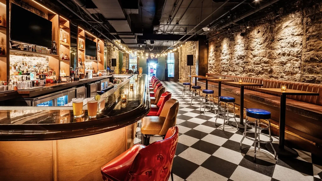 Empty bar with a curved wooden bar, bottles, and checkerboard floor.