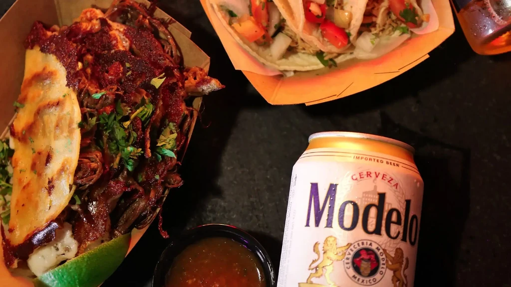 Top-down shot of birria, tacos, salsa, and Modelo beer.