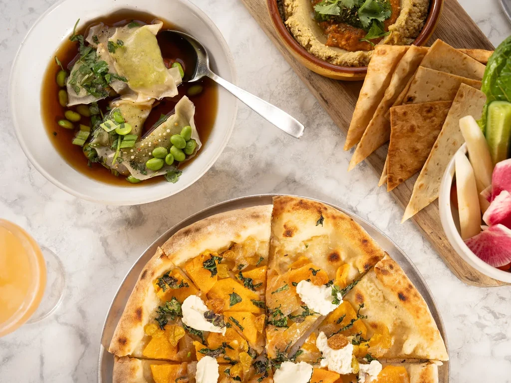 Dining table overhead with dumplings, hummus, pita, and pizza.