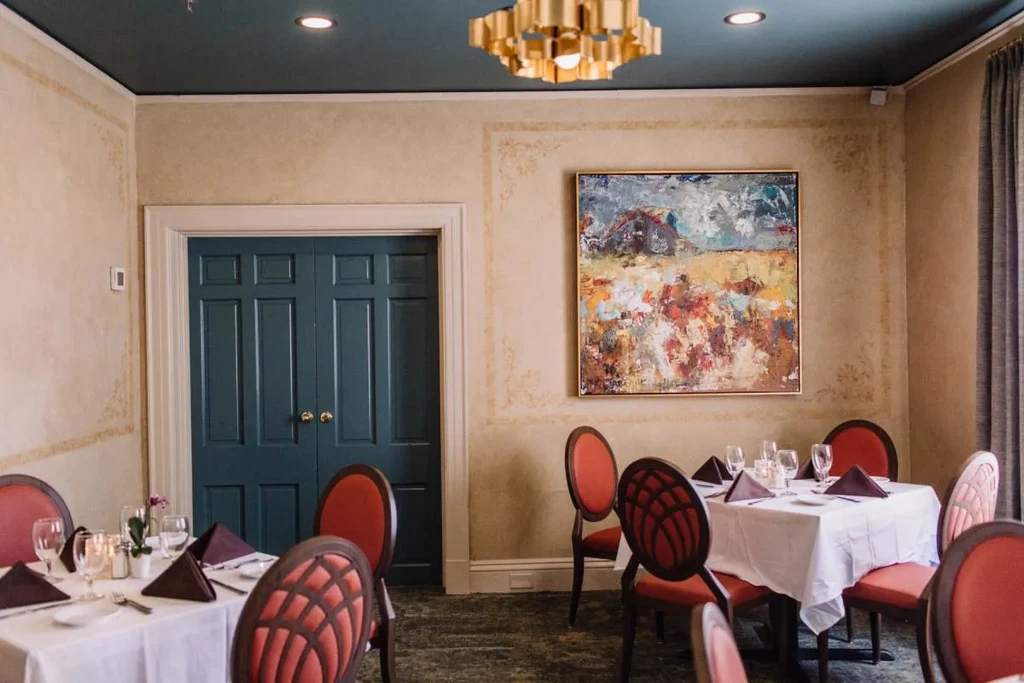Dining room interior features teal ceiling, gold chandelier, set tables, red chairs.