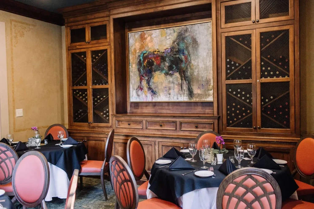 Restaurant dining room with set tables, wine storage, and horse painting.