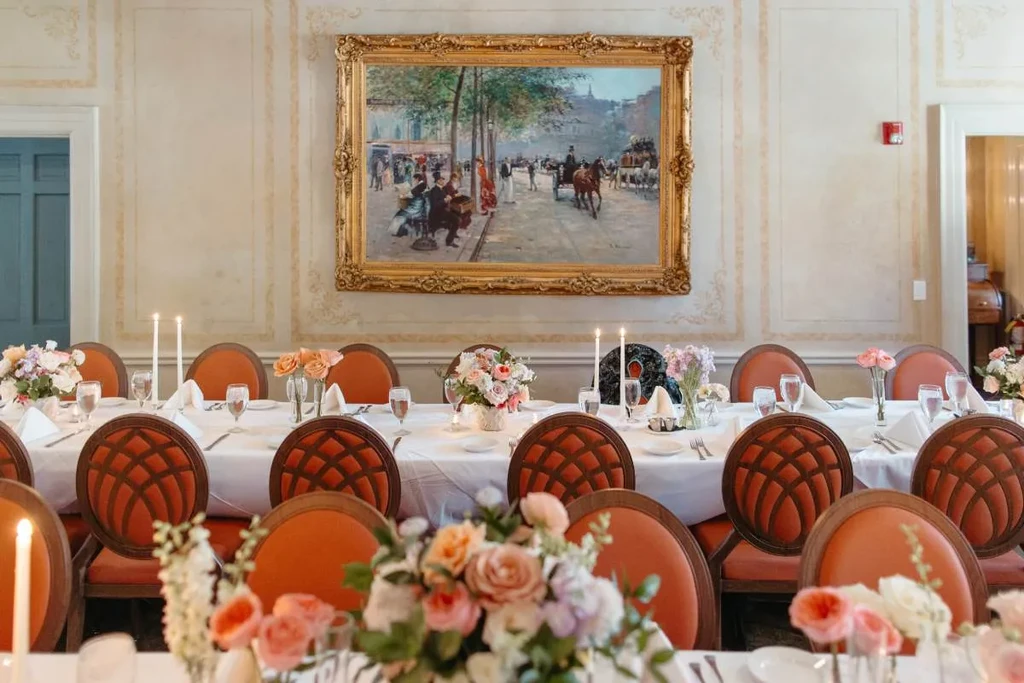 Formal dining room with table, flowers, candles, and ornate painting.