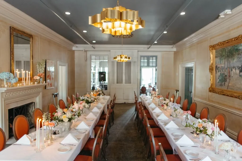 Elegant room with two long dining tables, orange chairs, chandeliers.