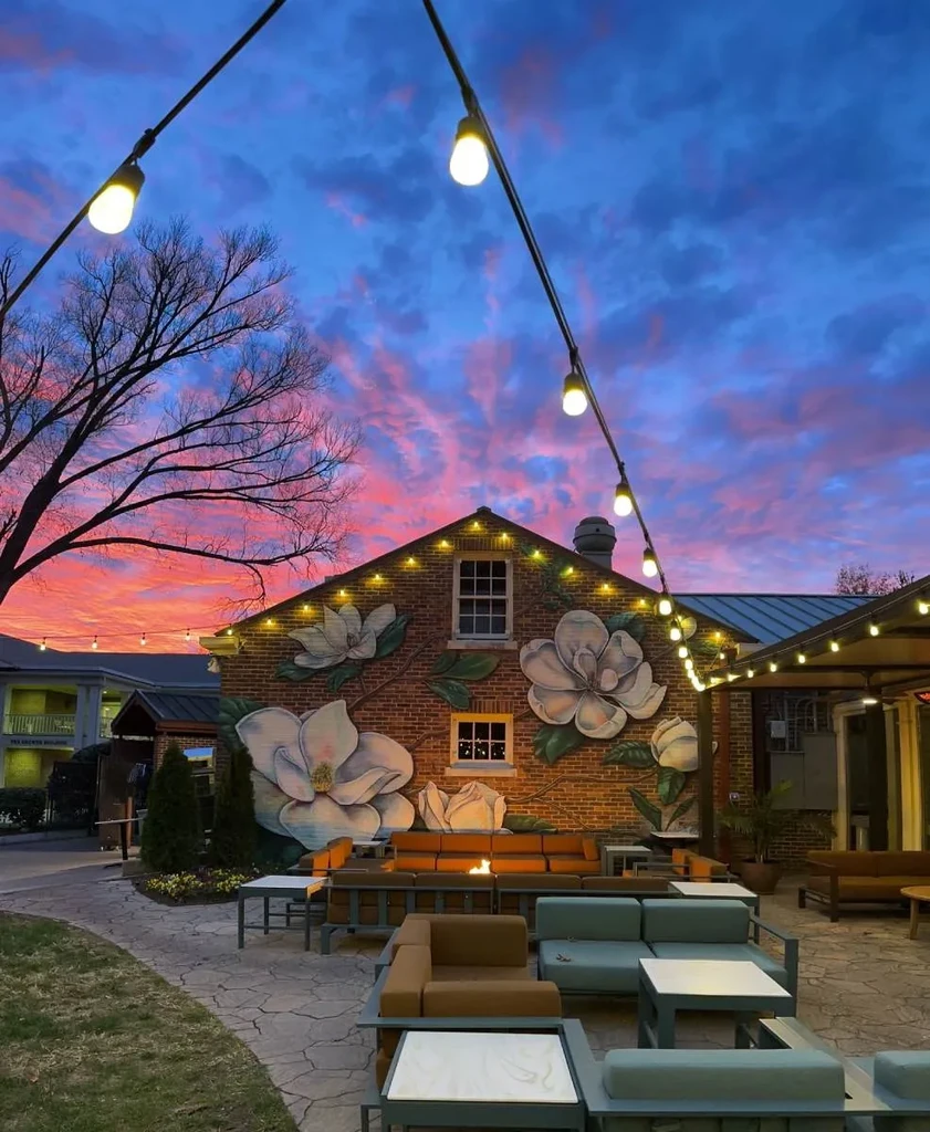 Patio with magnolia mural building, string lights, modern seating at sunset.