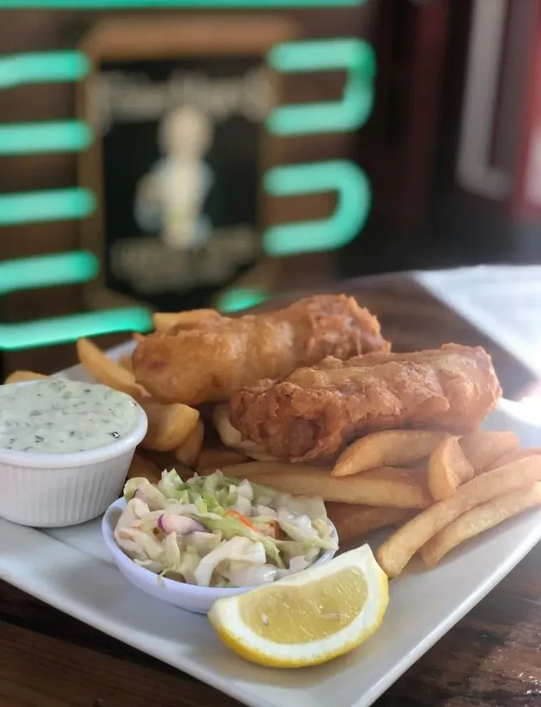 A plate of fish and chips with coleslaw, lemon, and tartar sauce.
