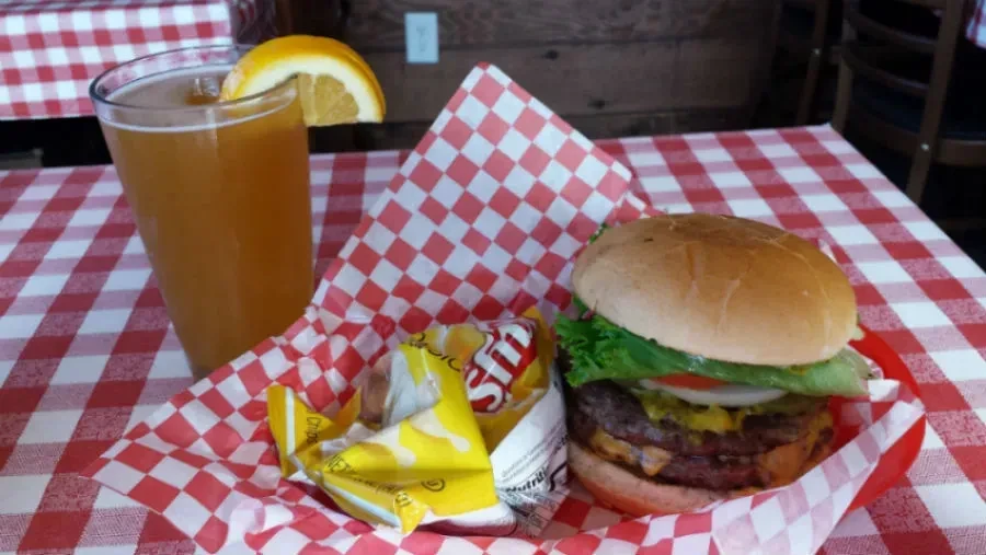 A burger, chips, and drink on a red and white checkered tablecloth.