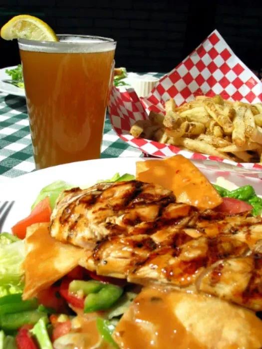 Grilled chicken salad with fries and a glass of beer outdoors.