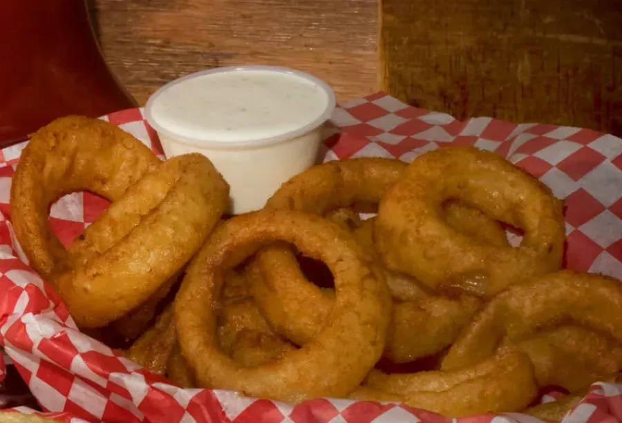 A basket of golden-brown onion rings with a side of dipping sauce.