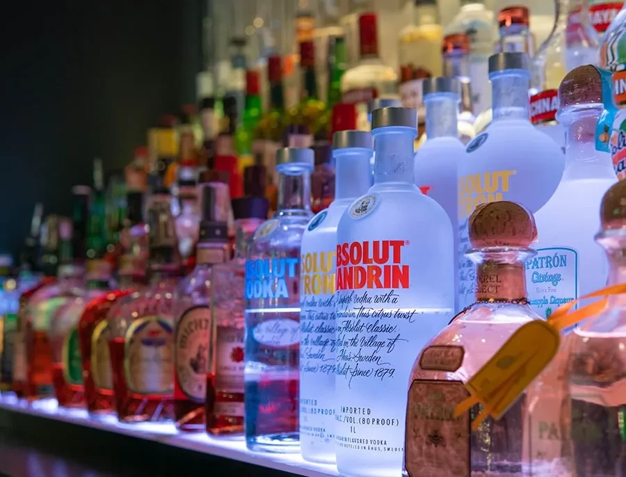 A backlit bar shelf displays multiple rows of various liquor bottles.