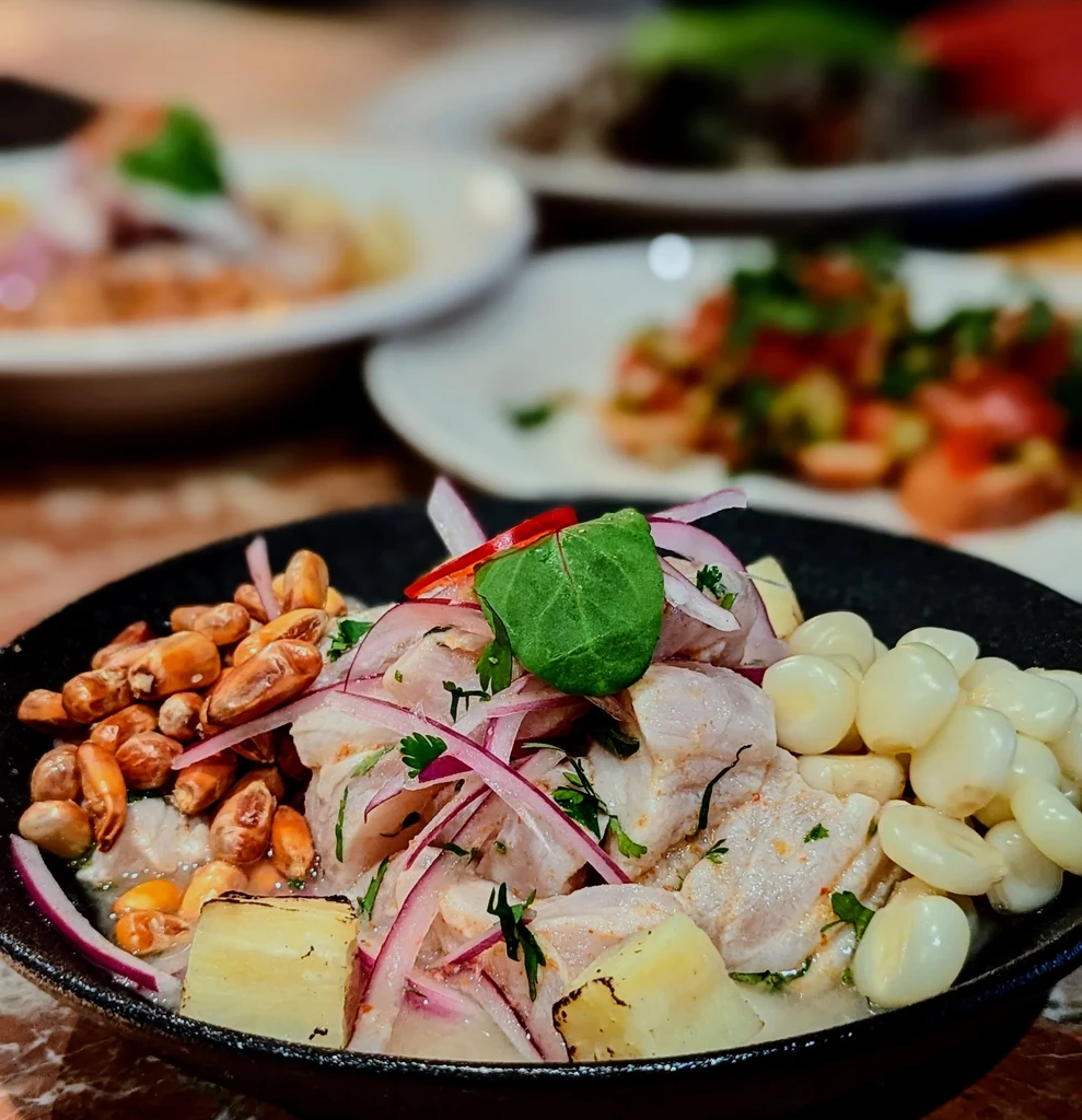 Ceviche with fish, red onion, corn, and cilantro in a black bowl.