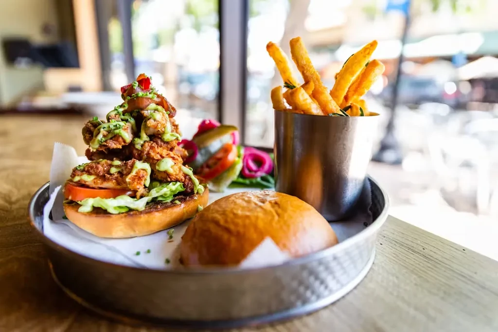 A fried chicken sandwich, fries, and pickles on a metal tray.