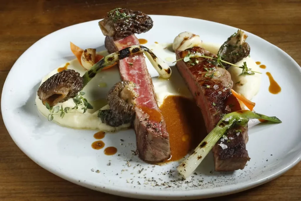 Two pieces of steak with mashed potatoes, mushrooms, and herbs.
