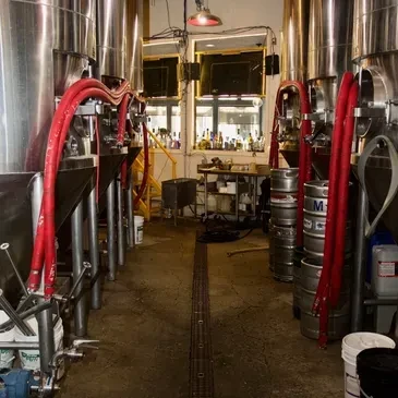 Large shiny brewing tanks with red hoses in a brewery.