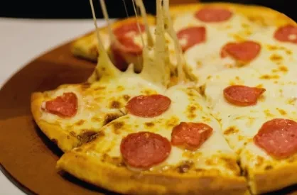 A pepperoni pizza on a wooden board with a slice being pulled.