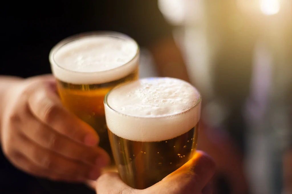 Two hands clinking two glasses of golden beer with foamy heads.