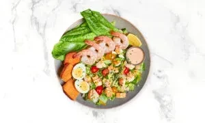 A shrimp salad with lettuce, sweet potato, egg, and dressing.