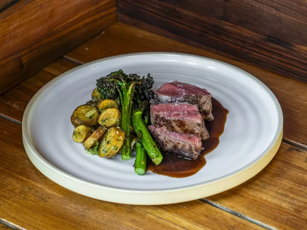 Sliced steak, asparagus, and roasted potatoes on a white plate.