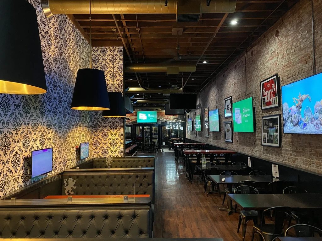 Long restaurant interior with booths, tables, and brick walls with TVs.