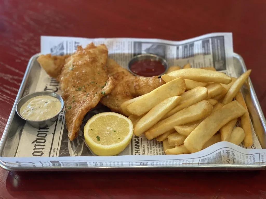 Fish and chips served on newspaper with lemon and dipping sauces.