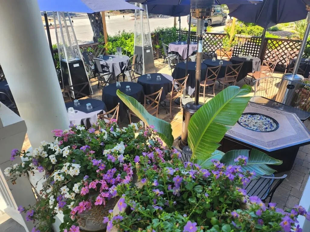 A restaurant patio with tables, chairs, umbrellas, and flowers.