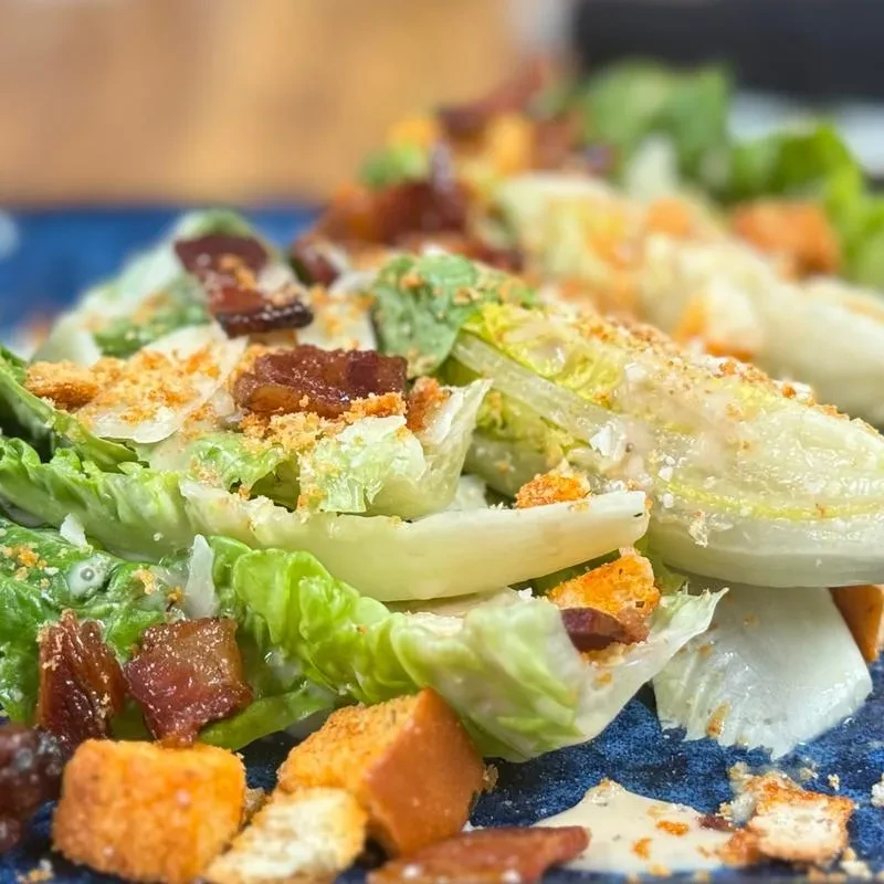 Close-up of a Caesar salad with bacon, croutons, and Parmesan cheese.