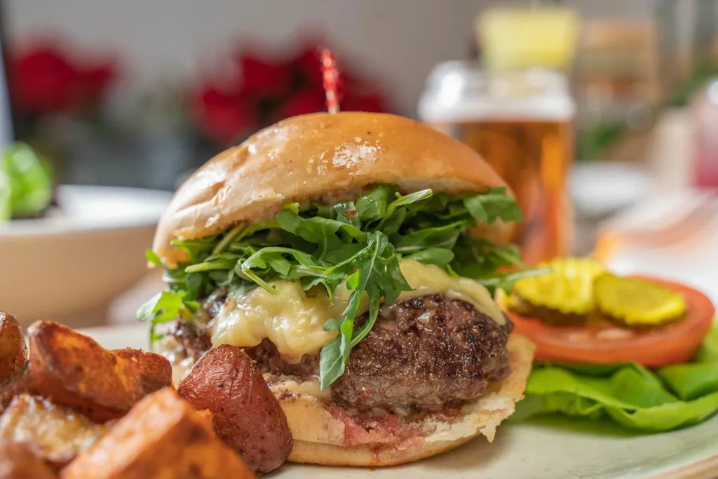 A cheeseburger with arugula, a side of potato wedges, and pickles.
