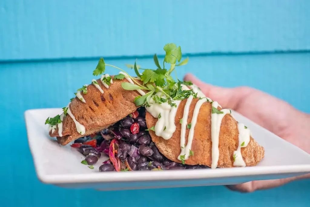 Two croissants with black beans, topped with sauce and herbs, on a white plate.