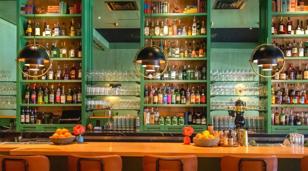 A long, light wood bar with shelves of liquor bottles and glasses.