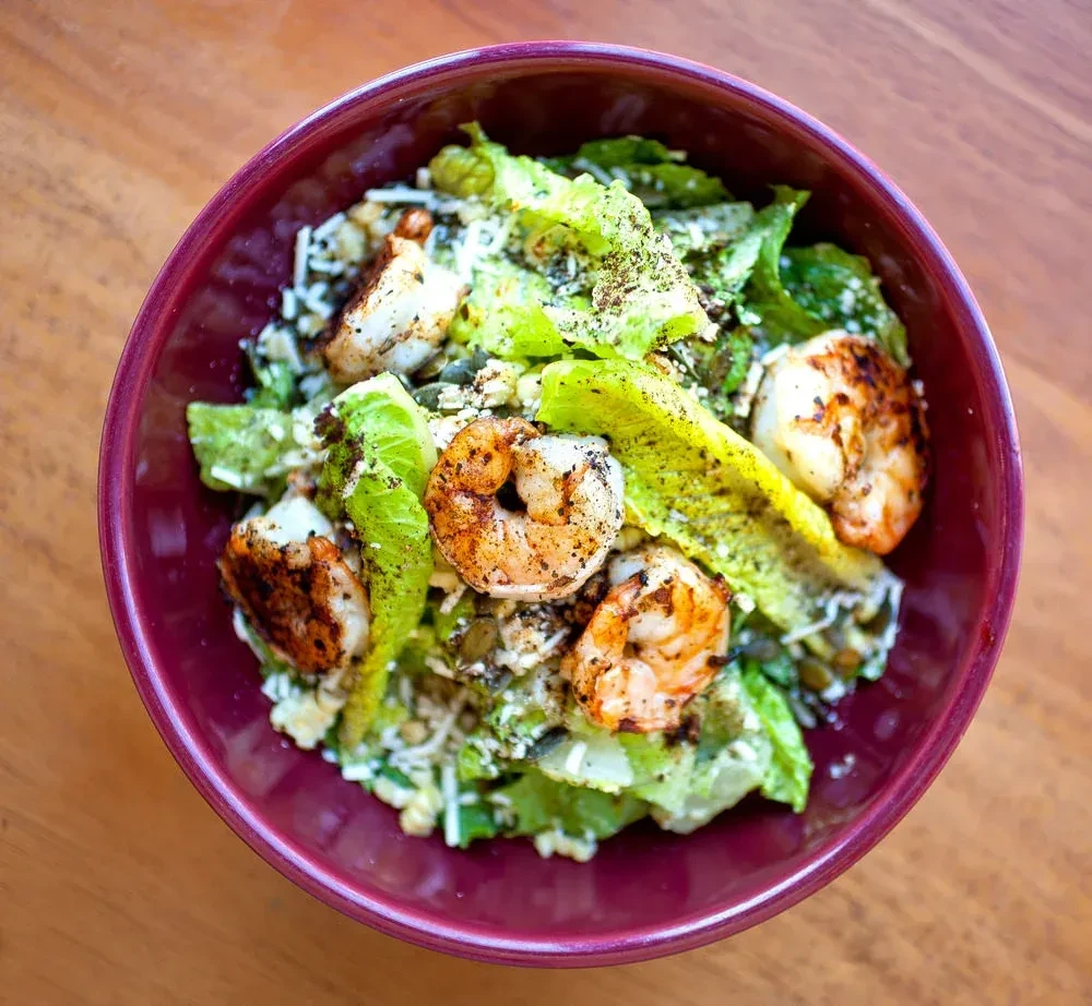 Overhead view of a vibrant shrimp salad in a maroon bowl.