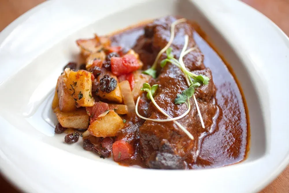 A plate of beef stew with potatoes, tomatoes, and raisins.