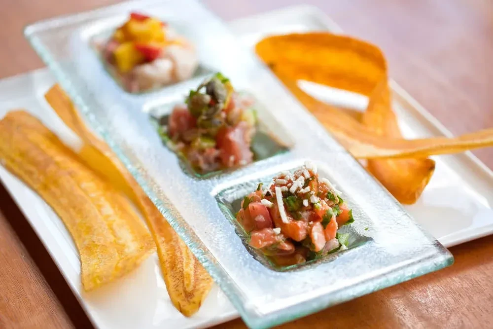 Three servings of ceviche on a glass tray with plantain chips.