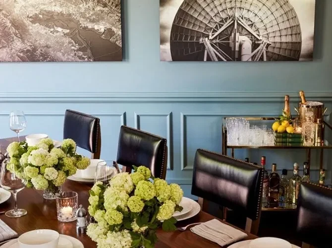 A dining room with a long table set with flowers and a bar cart.