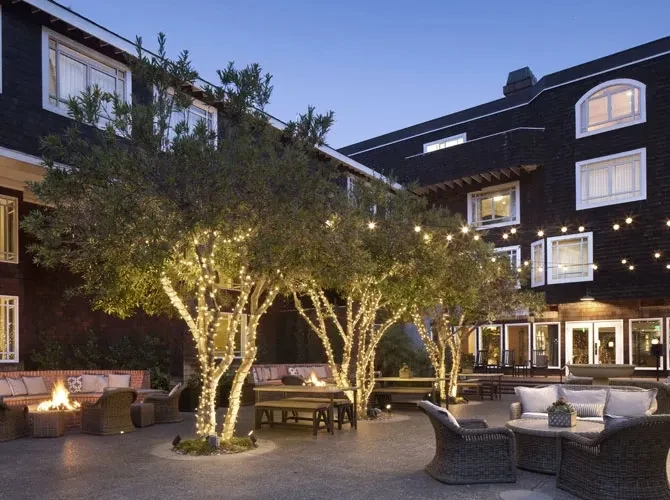 Courtyard patio with string lights, trees, fire pit, and outdoor seating at dusk.