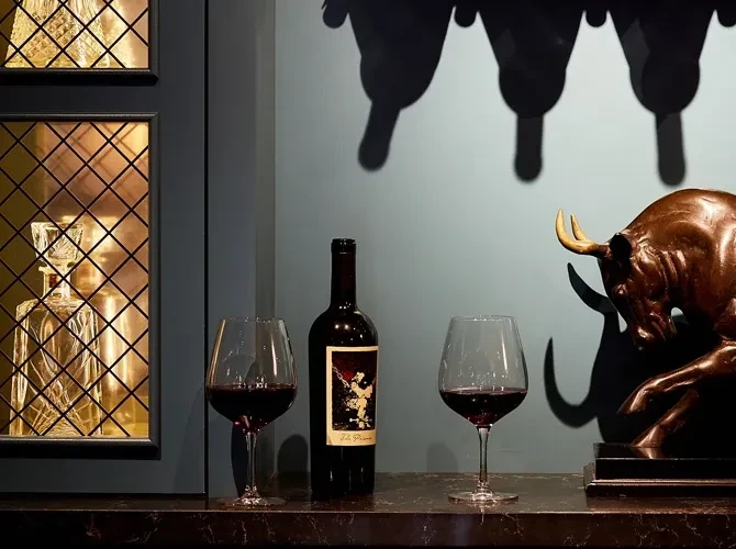 Red wine bottles, glasses, a decanter, and a bull statue.