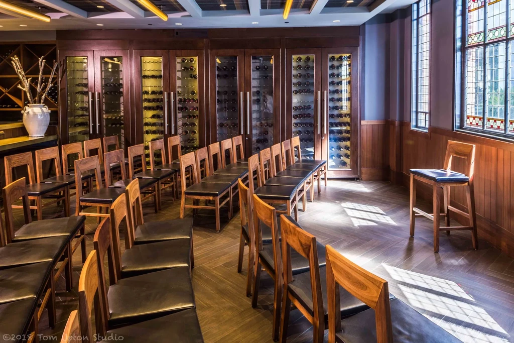 A room with wine storage, rows of chairs, and stained-glass windows.
