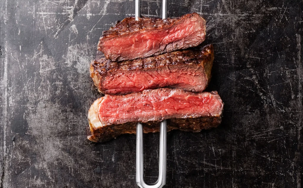 Three grilled medium-rare beef steaks on a metal fork, top-down view.