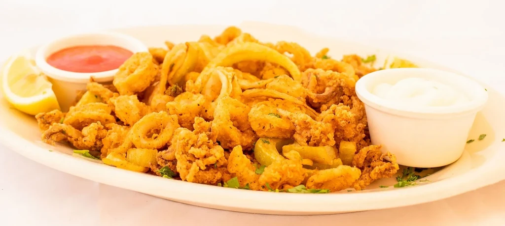 A platter of crispy fried calamari with two dipping sauces and a lemon wedge.